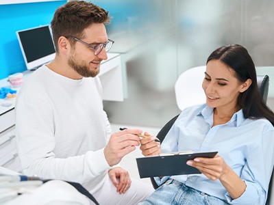 Dentist handing patient clipboard with forms to fill out