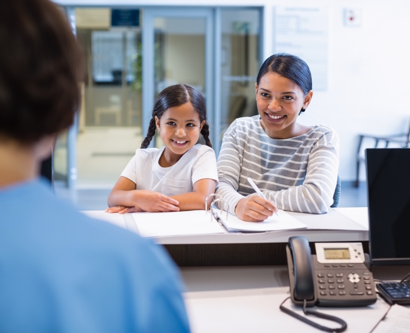 Mother and child completing dental insurance forms at dental office reception desk