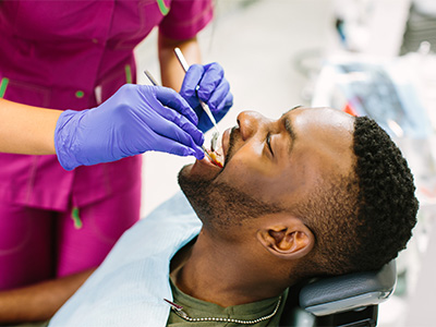 Dentist in magenta scrubs examining a man's mouth