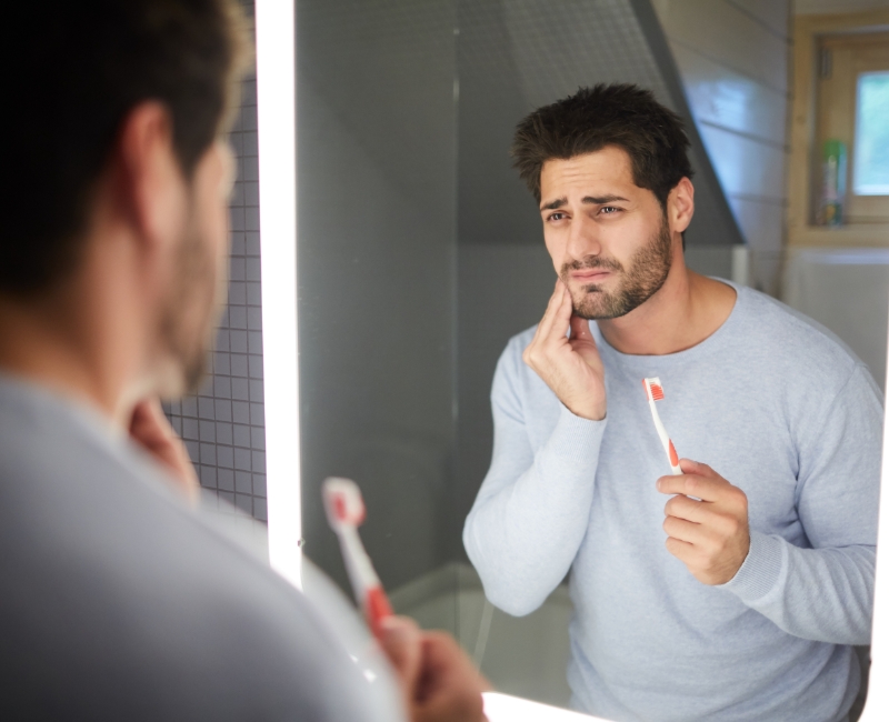 Man in need of emergency dentistry holding cheek in pain