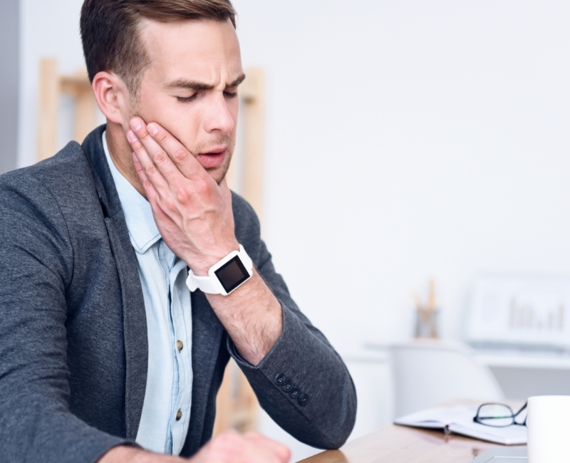 Man in need of T M J and bruxism therapy holding jaw