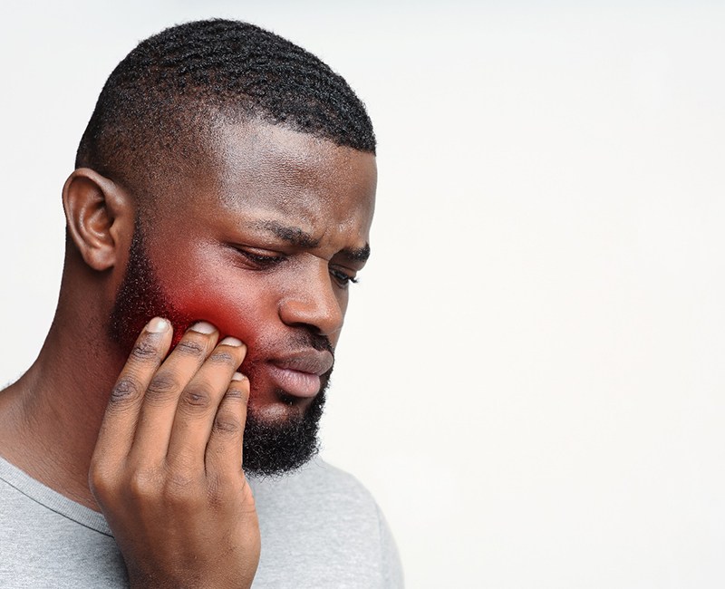 Man in grey shirt rubbing side of jaw in pain