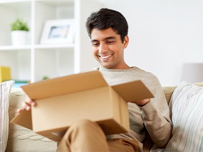 Man in neutral sweater on couch opening box smiling
