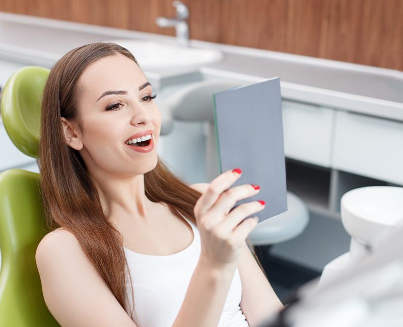 Female patient holding up mirror to check smile