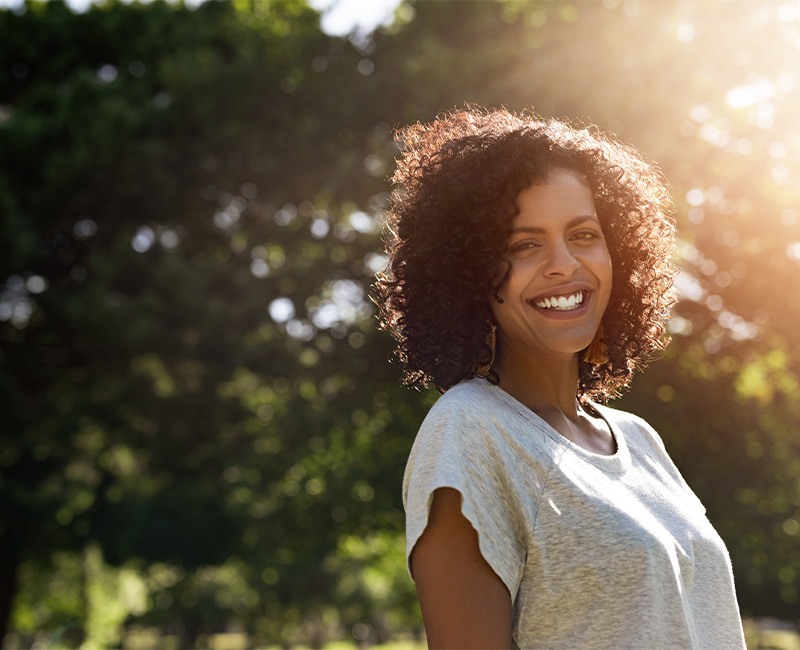 Woman with brown hair in gray shirt outside smiling