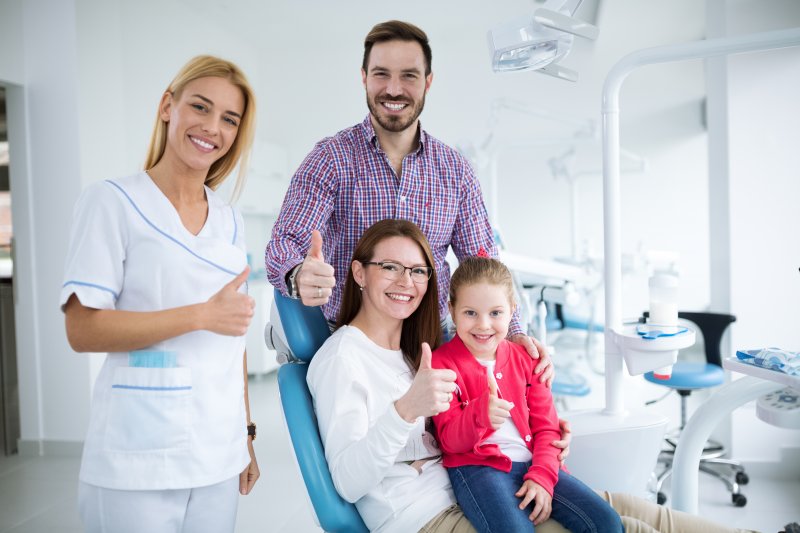 a husband, wife, and child giving a thumbs up while standing next to a family dentist 