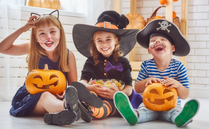 three small children all seated and holding pumpkins and Halloween candy 