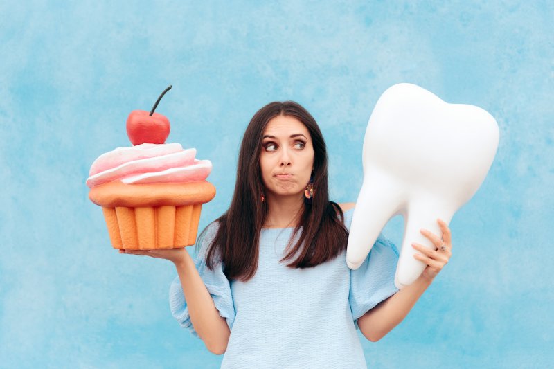 Woman holding fake tooth in one hand and cupcake in the other