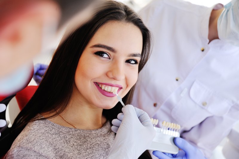 a young female smiles as a dentist uses a shade guide to determine the color of her veneers 