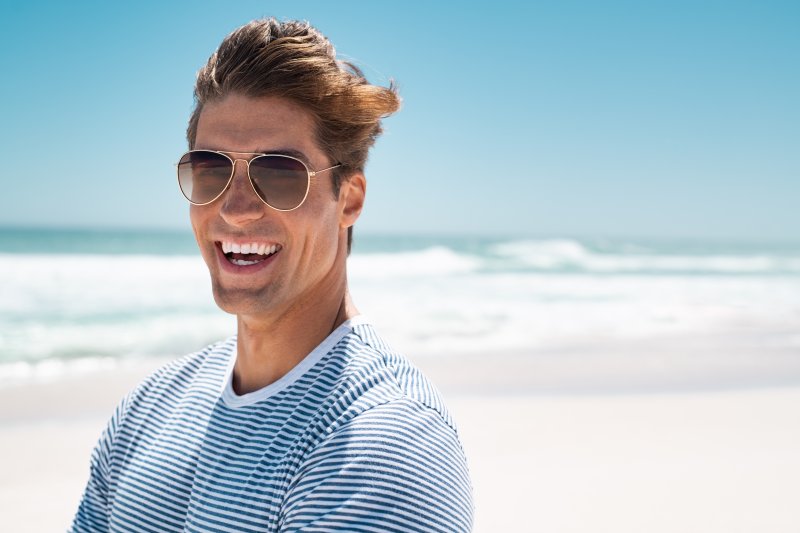 a man standing on the beach and smiling after taking steps to prevent dental emergencies in Rochester