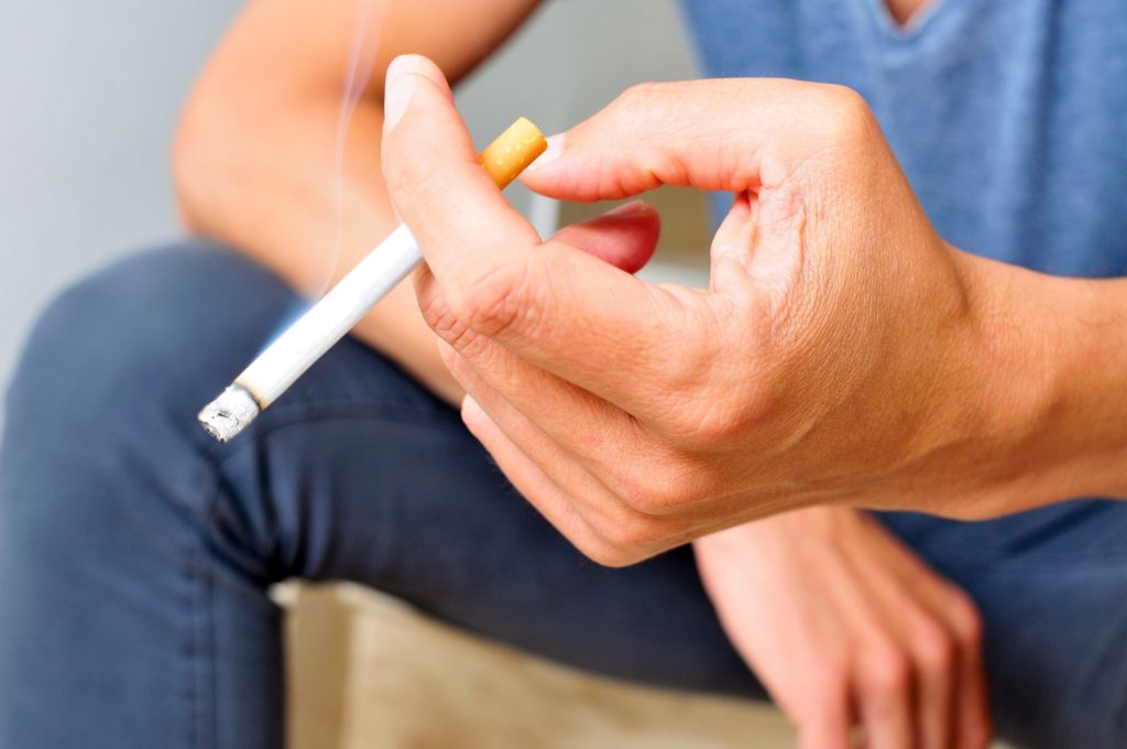 Closeup of person in blue shirt holding cigarette